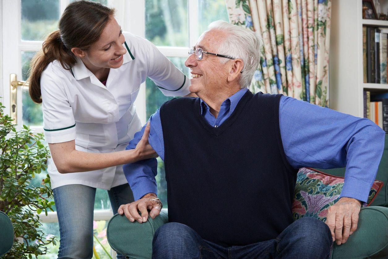 A woman is helping an older man sit in his chair.